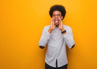 Young african american man over an orange wall shouting something happy to the front