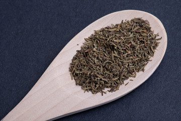 Heap of Dried Organic Culinary Thyme Herb in handmade wooden spoon on dark background. Thymus vulgaris.