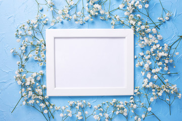 Empty  white frame and  fresh white gypsofila  flowers on blue textured background.