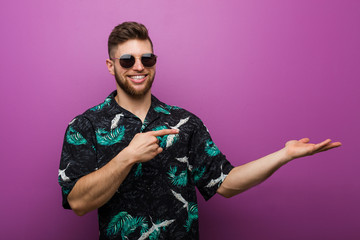 Young man wearing a vacation look excited holding a copy space on palm.