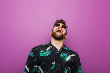 Young man wearing a vacation look relaxed and happy laughing, neck stretched showing teeth.