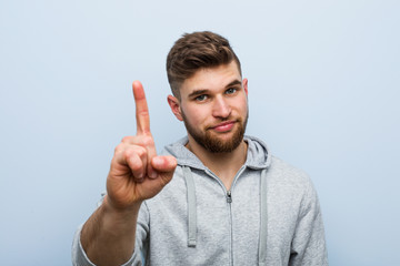 Young handsome fitness man showing number one with finger.