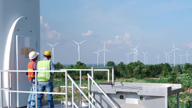 Two Asian engineers are checking the operation of wind turbines in wind farm field for production of electric power