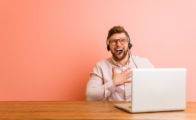 Young man working in a call center laughs out loudly keeping hand on chest.