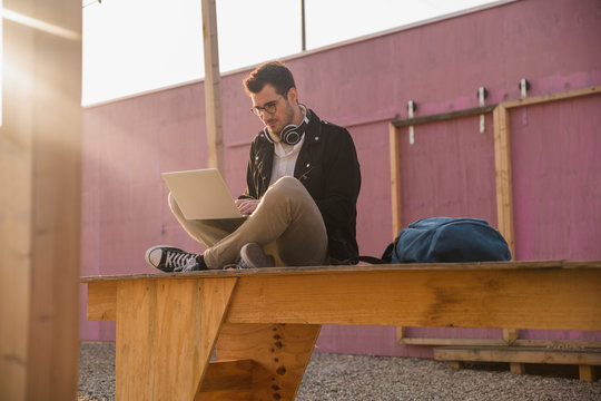 Young man sitting on platform using laptop