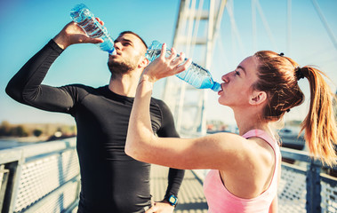 Rest after exercising. Thirsty sportsman and sportswoman drinking water after training outdoors....