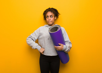 Young fitness black woman thinking about an idea. Holding a mat.