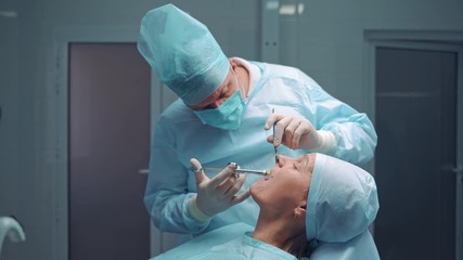 Dentist in medical clothes is doing anesthetic injection in the sick tooth. Stomatologist man treating female patient in the dentist office. Stomatology anesthesia