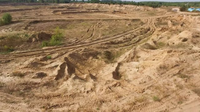 Aerial for the red big truck driving in ground quarry with flying dust behind it, industry concept. Scene. Empty lorry moving on country road with green forest on the background.