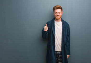 Young redhead man in pajama smiling and raising thumb up