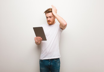 Young redhead man worried and overwhelmed. Holding a tablet.