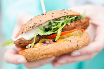 Vegetarian steak burger with lettuce, tomato, cucumber pickle, cheese & mayonnaise, female hands