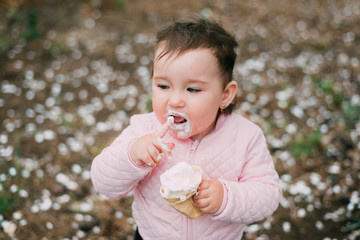 little girl in the garden on the background of greenery and trees very cute eating ice cream finger in a waffle Cup