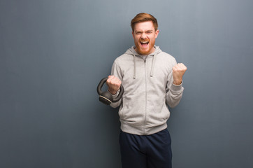 Young redhead fitness man surprised and shocked. Holding a dumbbell.