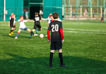 Boys in white and black sportswear plays  football on field, dribbles ball. Young soccer players with ball on green grass. Training, football, active lifestyle for kids concept 