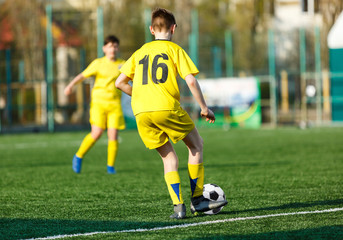 Obraz premium Football teams boys in yellow white sportswear play soccer on the green field. Dribbling skills. Team game, Training, active lifestyle, hobby, sport for kids concept