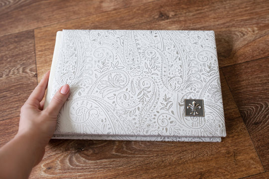 Photo book with a cover of genuine leather. White color with decorative stamping. Photo book in woman hand