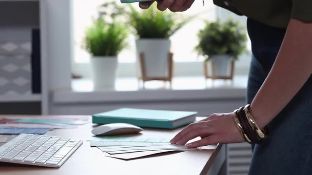 Young woman holds the color samples. She takes a picture of them with her phone and sends them to the client to look at. She wears nice trendy sweater