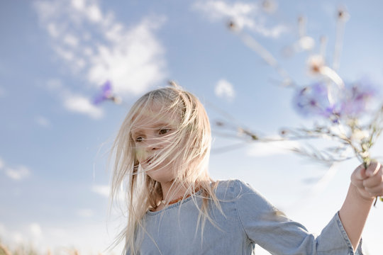 Blond girl with windswept hair holding cornflowers