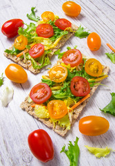 Healthy snack from wholegrain rye crispbread cracker with cherry tomatoes, avocado and salad. Proper nutrition.