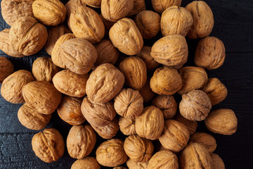 WALNUT NUTS IN A SHELL SPREADED ON A COAL BLACK WOODEN BACKGROUND FLAT LAY