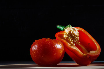 RED TOMATO AND HALF OF Sweet pepper IN DROPS OF WATER LAY ON THE CUTTING BOARD ON THE BLACK BACKGROUND FRONT VIEW
