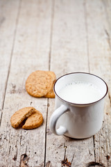 Cup of milk and some fresh baked oat cookies on rustic wooden table background.