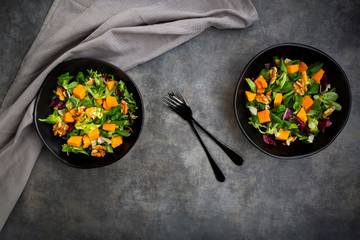 Two bowls of mixed green salad with Hokkaido pumpkin and walnuts