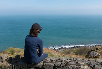 Woman looking at ocean back to camera, sunny day
