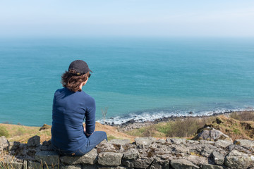 Naklejka na ściany i meble Woman looking at ocean back to camera, sunny day