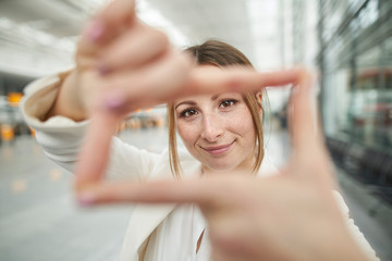 Portrait of smiling young businesswoman doing finger frame at the airport