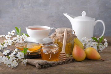 Jars with honey, pears, cherry blossoms, a cup of tea with a kettle on the table.