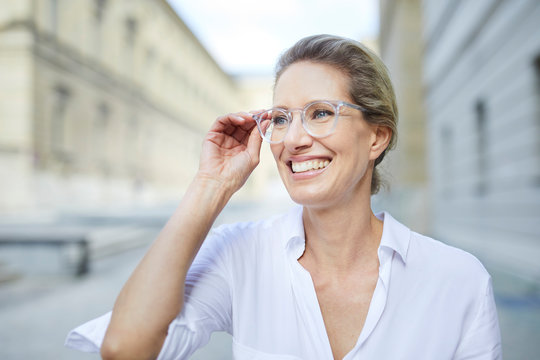 Portrait of smiling woman wearing white shirt and glasses in the city