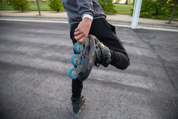 Crop back view of young cool man in sportswear holding roller skate with hand on road in park
