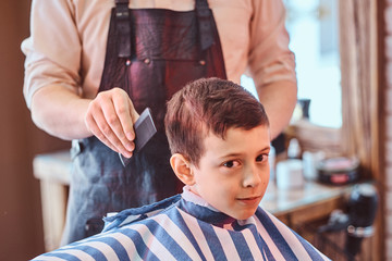 Small pretty school boy had his first trendy haircut at modern barbershop.