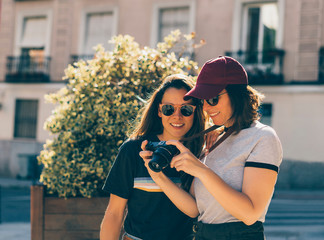 A couple of gay woman sightseeing together, smiling and looking his reflex photo camera. Same sex young married female couple showing some affection LGBT in Madrid.
