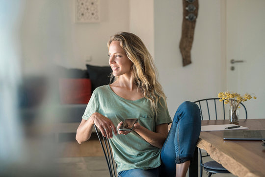 Smiling Woman With Cell Phone And Laptop On Dining Table At Home