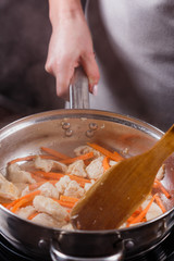young woman in a gray aprons roasts chicken fillet with carrots