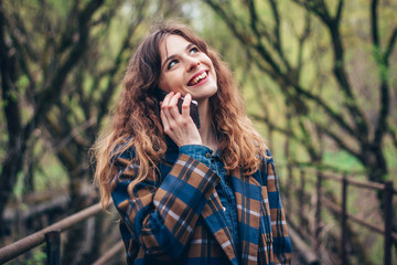 Excited young woman talking on cell phone in park.