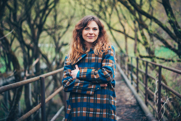 Attractive girl with curly hair  wrapped in a coat. Young woman in autumn park. Stay warm concept.