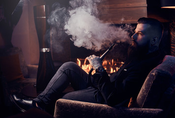 Obraz premium Elegant smart man is relaxing and smoking hookah after long hard day.