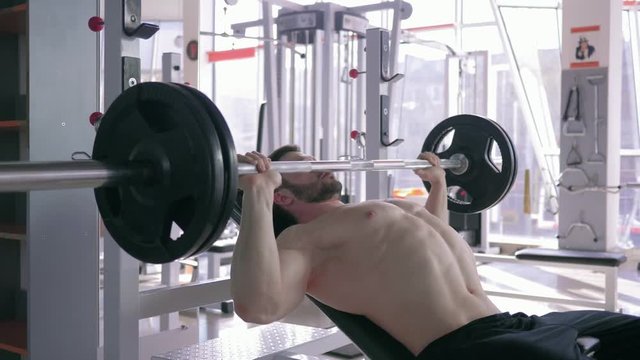 strong muscular sports male bare-chested doing bench press with barbell while power working out in gym