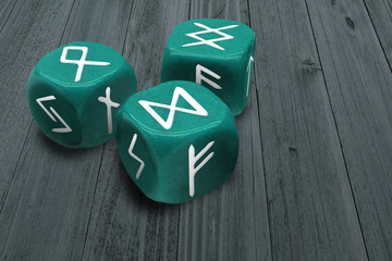 Fortunetelling or Horoscope charting concept. Three dices with Runes signs symbols on faces. Prediction or astrology medium esoteric stuff. Macro of green gambling cubes on wooden table background