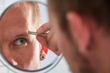 Junger Mann zupft Augenbrauen