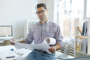Portrait of young engineer looking at camera while working in office behind glass, copy space