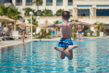 Naklejka premium Boy having fun on summer vacation. He is making jump into swimming pool with crossed legs and arms wide open.