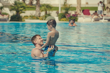 Dad is holding his son in his arms, while having fun in the luxurious pool.