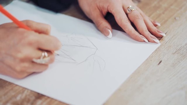 Young woman's hands of a fashion designer drawing sketches of clothes in the atelier. Female tailor draws with a sharp pencil indoors. Close-up