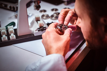 Mature watchmaker is doing engraving for custmer's watch at his workshop.