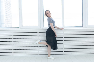 Youth, style and people concept - young woman on black skirt and sneakers standing near the window